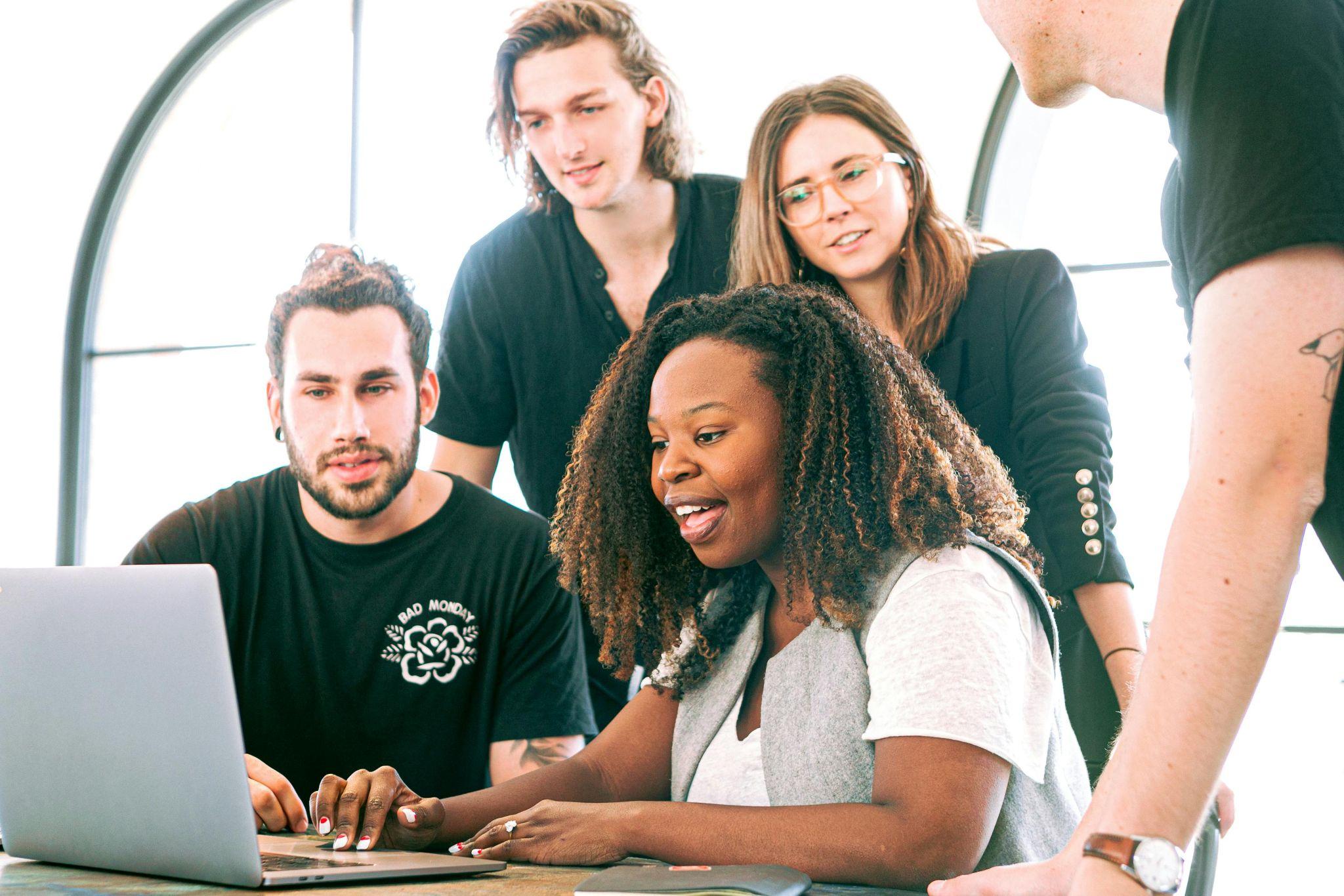 A diverse group of young professionals collaborating around a laptop, discussing employee benefits options
