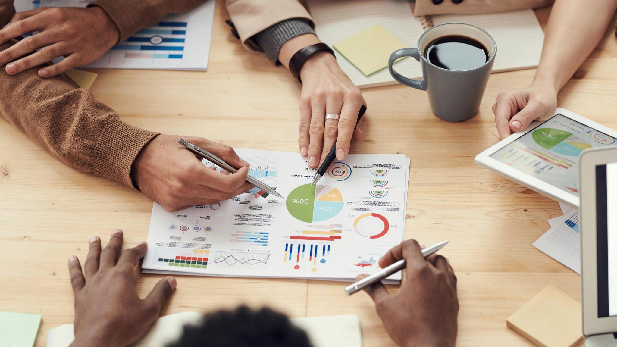 Close-up of hands pointing at financial and pie charts on paper, reviewing employee benefits and payroll data.