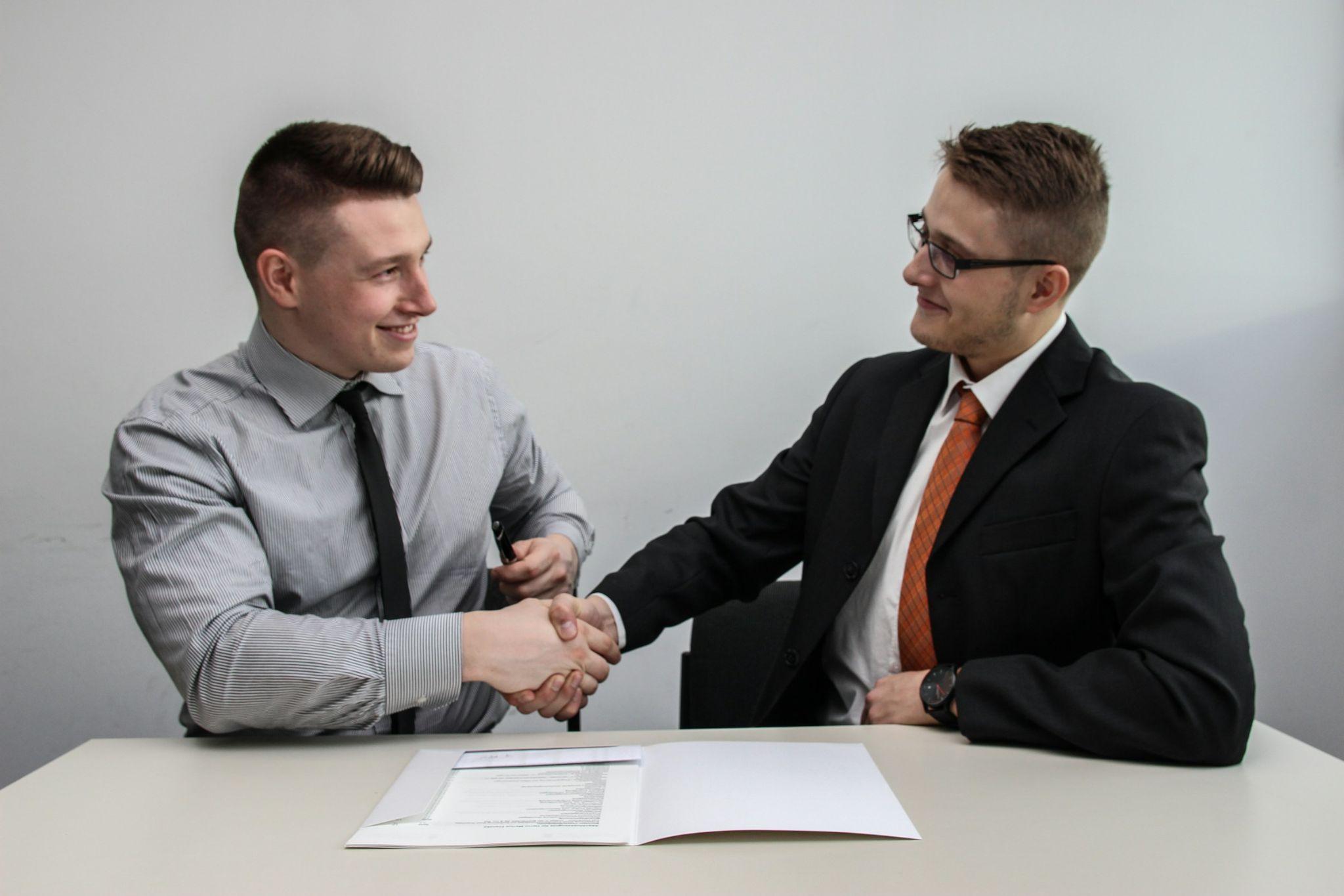 Two professionals in formal attire shaking hands after a successful business discussion about PEO employee benefits