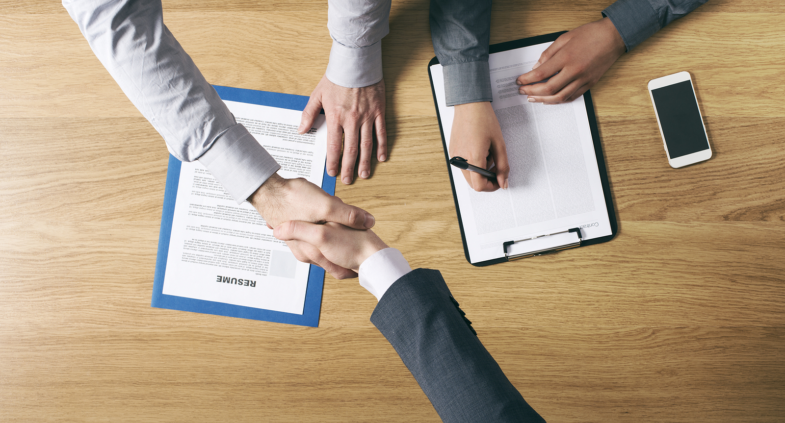 Employer and new hire completing paperwork and shaking hands, representing traditional corporate training and employee training methods.